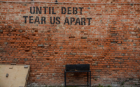 until debt tear us apart written on a red brick wall